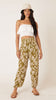 A model wearing green harem pants with a floral print, paired with a white top and a hat.